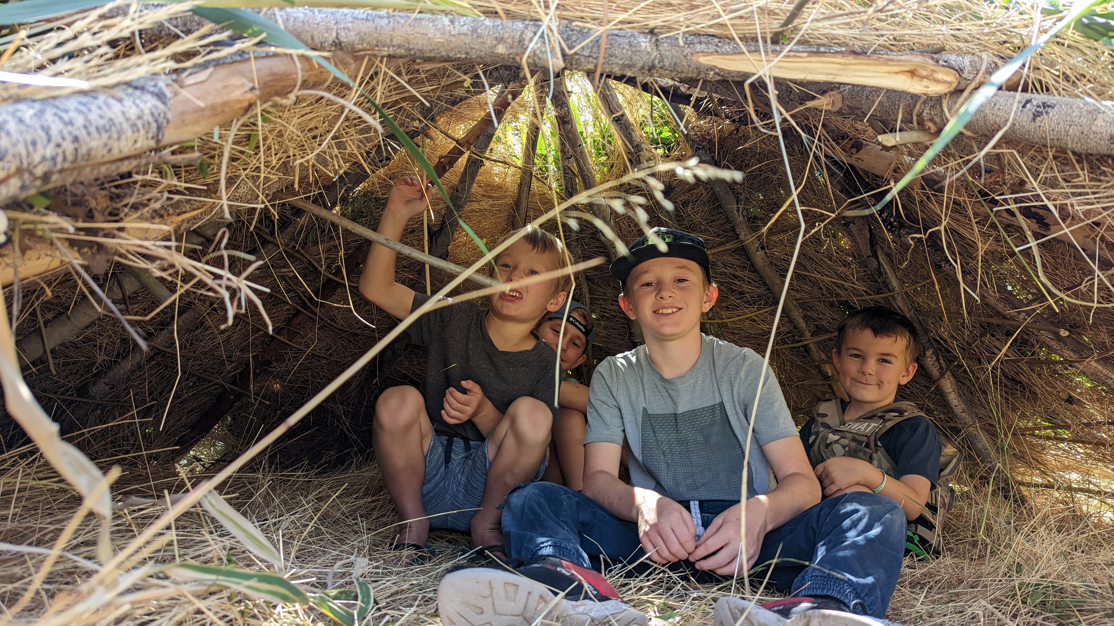 Kids sitting inside a debris shelter they built